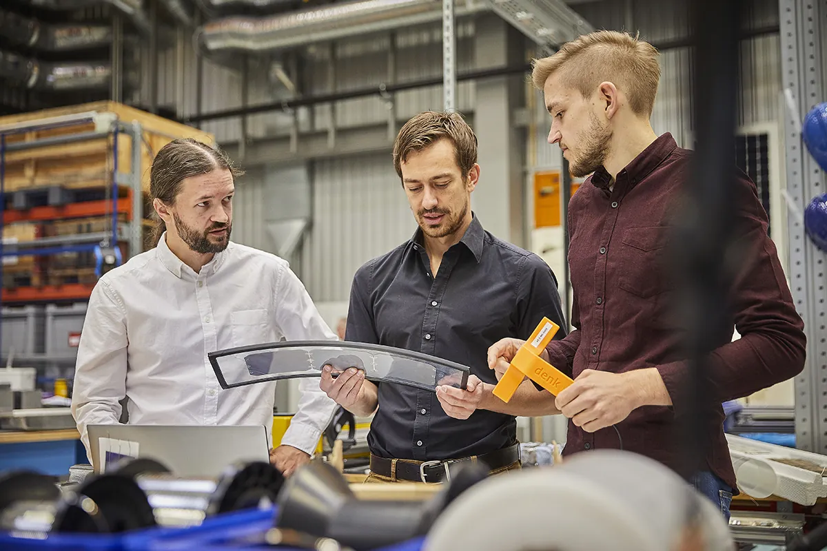 Three DENKweit employees examining a component in the workshop